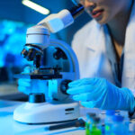 A woman in a lab coat is using a microscope to examine a sample. Concept of scientific curiosity and precision, as the woman carefully adjusts the microscope to get a clear view of the sample